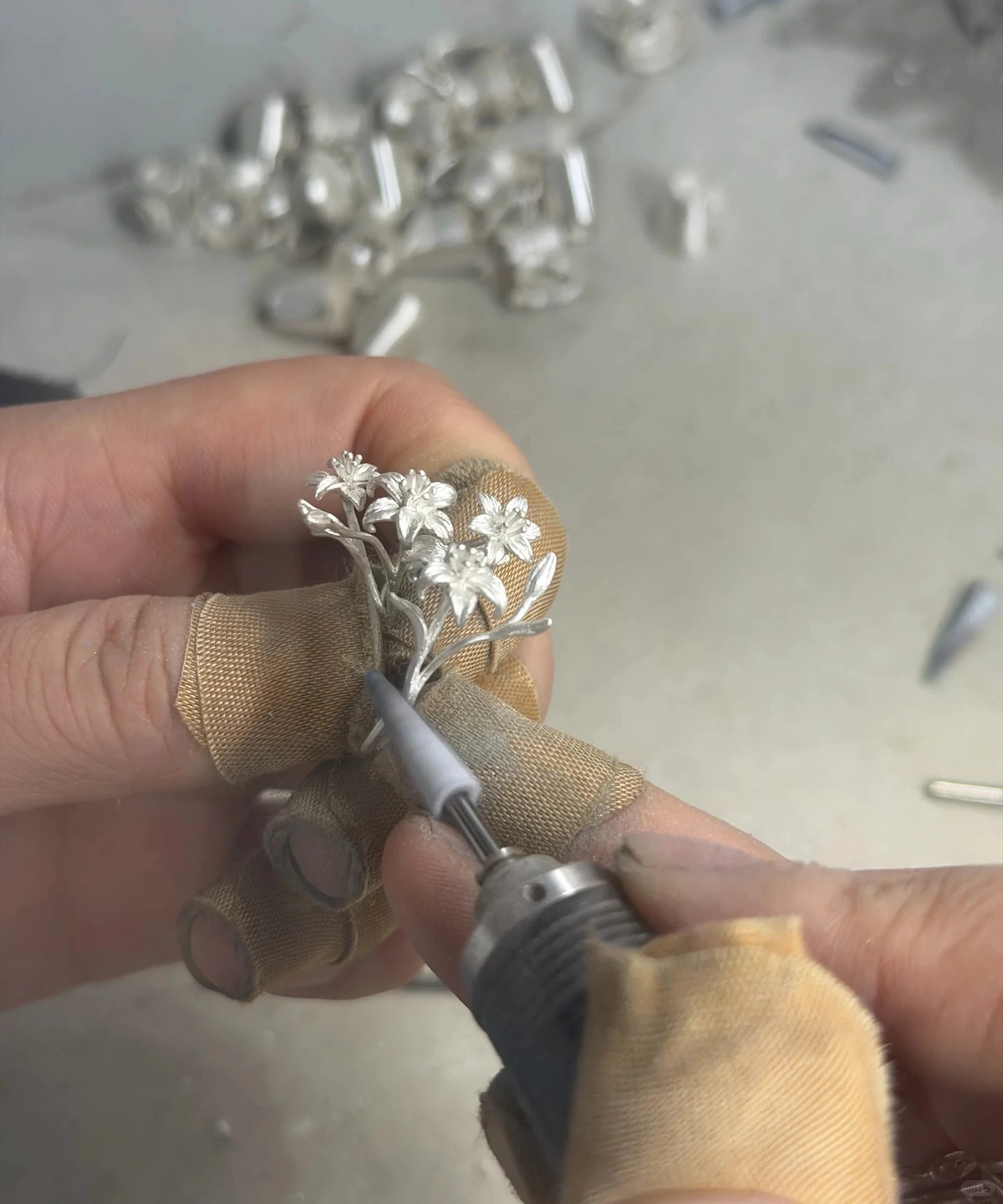A maker holding the silver lily ring while working on a stem with a rotary tool