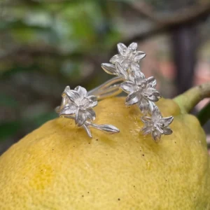 Matte silver lily ring resting on a yellow fruit, with four flowers and curved stems