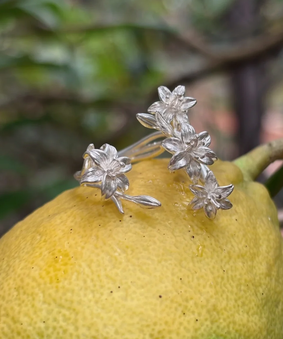 Matte silver lily ring resting on a yellow fruit, with four flowers and curved stems
