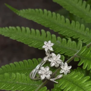 Silver ring with four lily flowers resting on overlapping green fern fronds