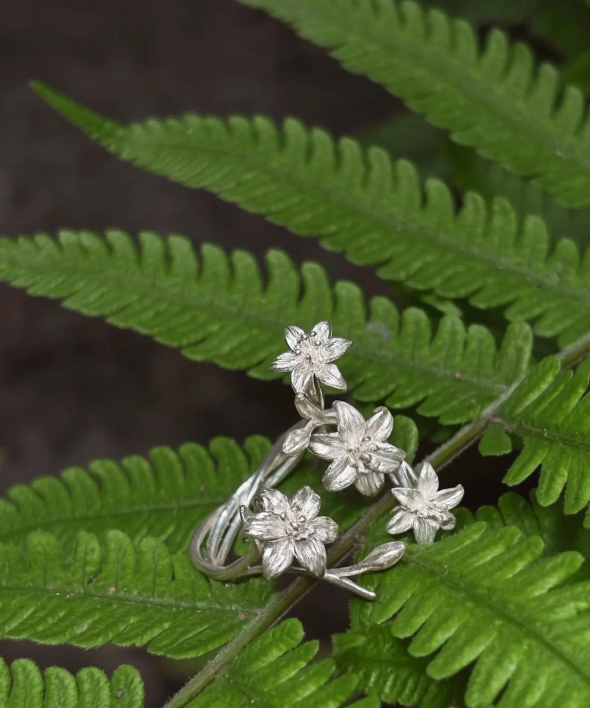 Silver ring with four lily flowers resting on overlapping green fern fronds