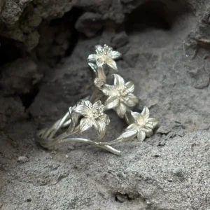 Silver lily ring on grey stone, showing raised flowers and curved stems from the side