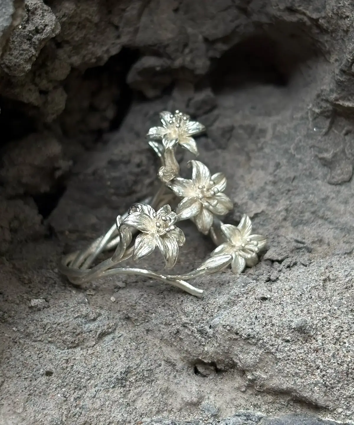 Silver lily ring on grey stone, showing raised flowers and curved stems from the side