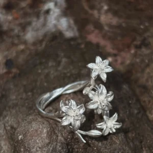 Open silver lily ring on textured brown bark, with the band visible behind the flowers