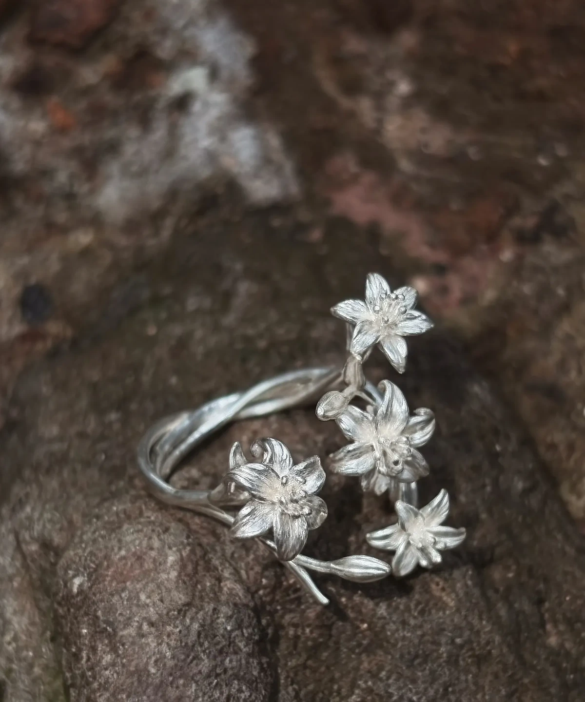 Open silver lily ring on textured brown bark, with the band visible behind the flowers
