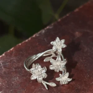 Close view of four silver lily flowers with grooved petals and rounded stamens on red stone