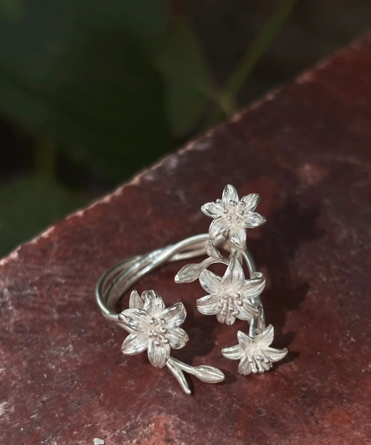 Close view of four silver lily flowers with grooved petals and rounded stamens on red stone