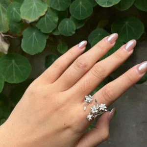 Polished-finish silver lily ring worn on a hand beside round green leaves