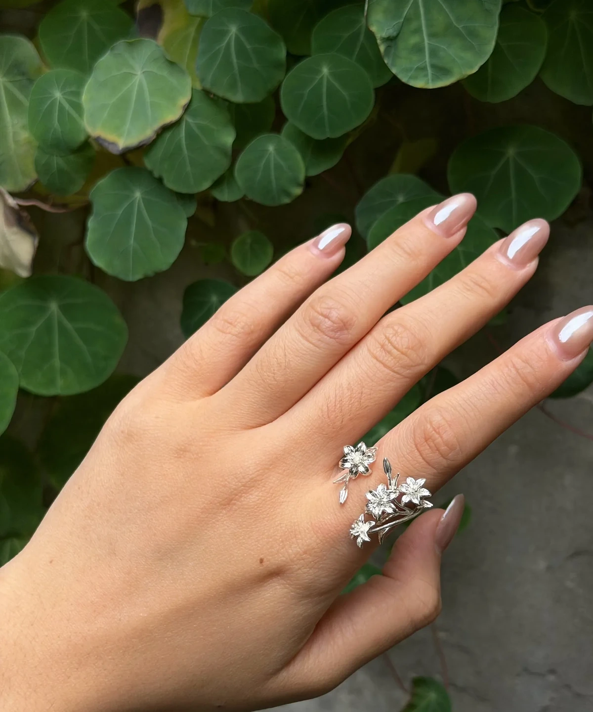 Polished-finish silver lily ring worn on a hand beside round green leaves