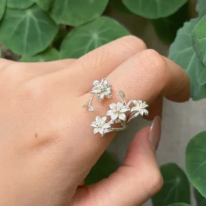 Open flower ring worn on a finger, with four silver lilies and buds against green leaves
