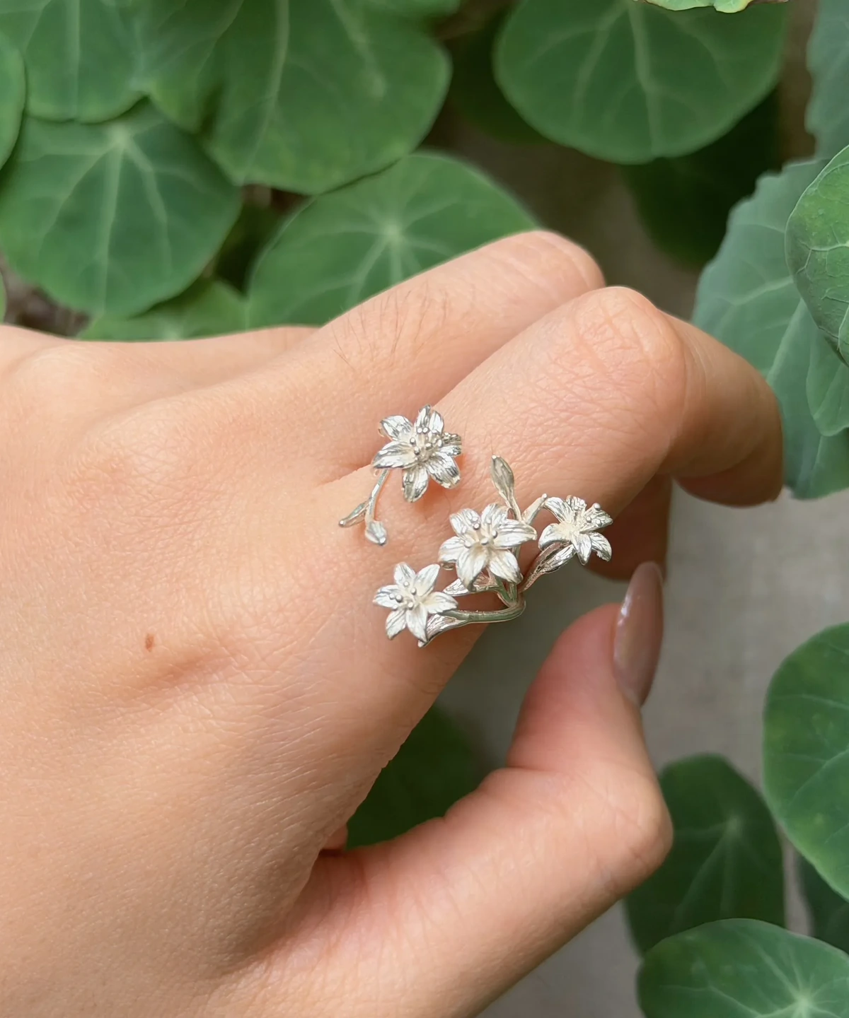 Open flower ring worn on a finger, with four silver lilies and buds against green leaves