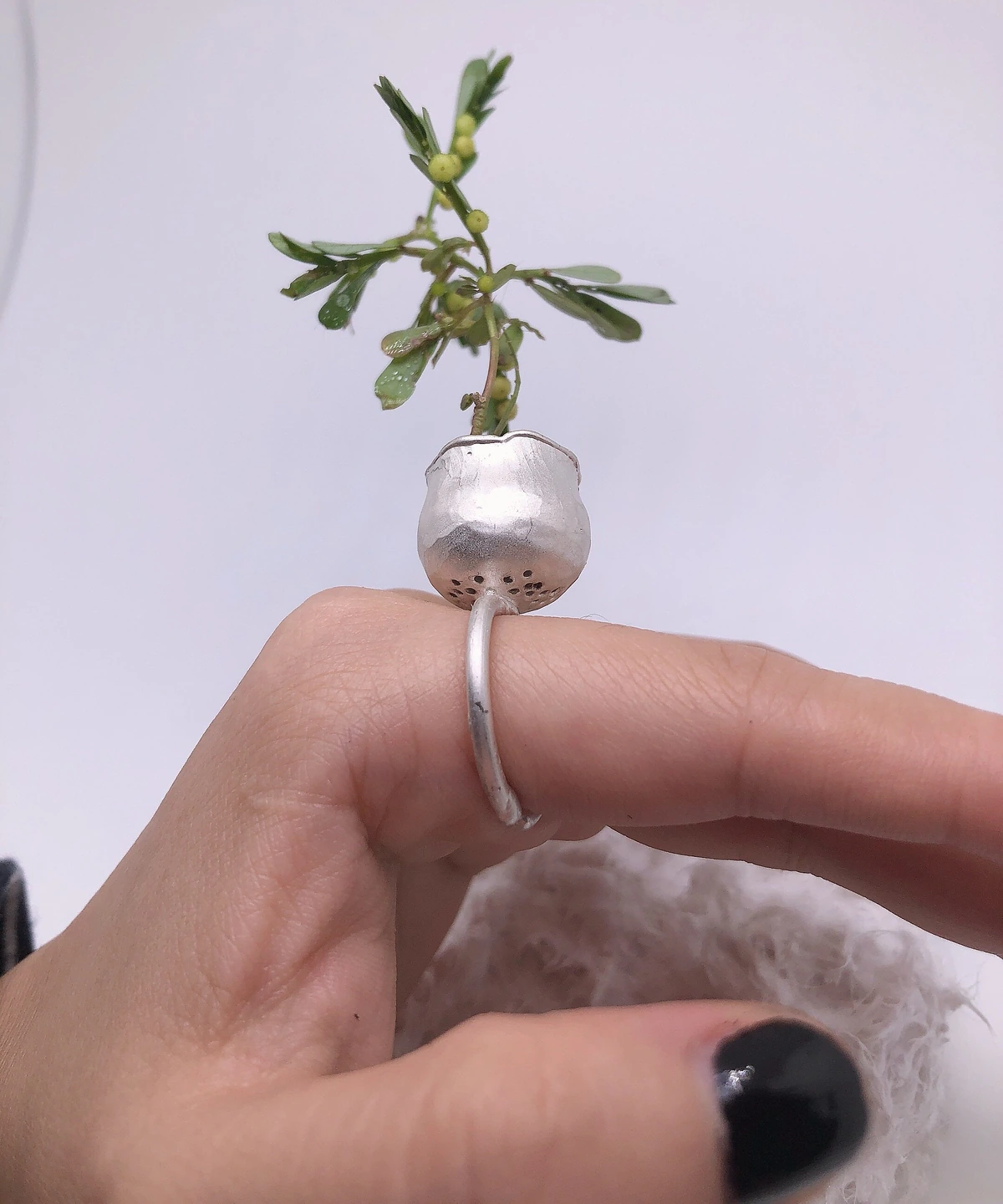 Side view of a silver planter ring showing small holes beneath the pot and the open ring band