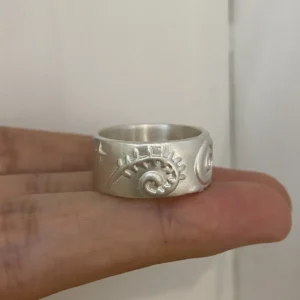 Curled botanical relief on the side of a wide silver ring held across the fingers.