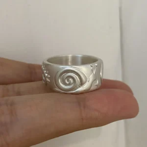 Silver snail ring with a matte wide band, raised spiral shell and antennae, held across the fingers.
