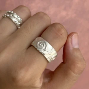 Raised spiral snail ring worn on a hand against a pink background beside a beaded silver ring.