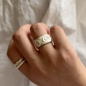Matte silver snail band worn on a hand against pale linen, with a slim ring on another finger.