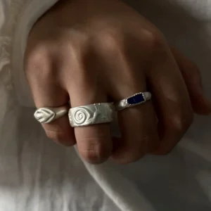 Wide snail band worn between a slim organic silver ring and a dark blue stone ring.