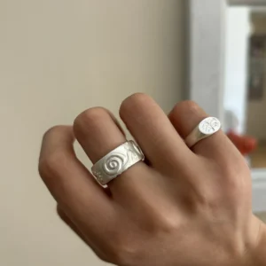 Wide silver ring with a raised snail worn beside a round botanical signet ring.