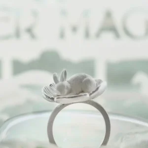 Rabbit flower ring standing on clear glass, showing the open band beneath the cupped flower.