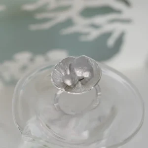 Overhead view of the silver rabbit flower ring on clear glass, showing the rabbit framed by textured petals.