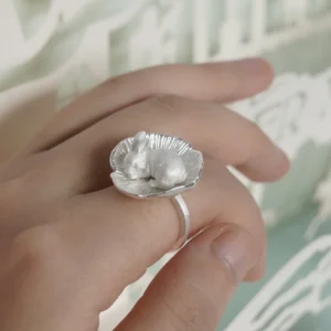 Angled view of the rabbit flower ring on a finger, showing the raised figure and narrow band.