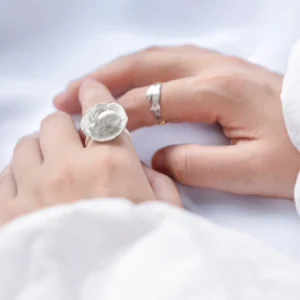 Rabbit flower ring worn on relaxed hands resting on white fabric, with another ring visible nearby.