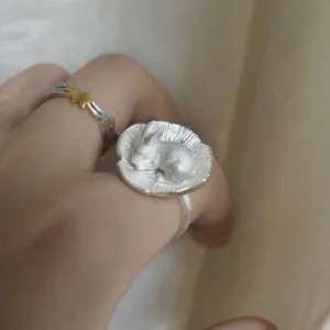 Rabbit flower ring worn on a curled hand against a pale background, with a separate star ring nearby.