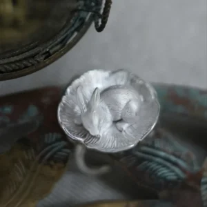 Close-up of a sleeping silver rabbit with long ears and tucked paws inside a textured flower.
