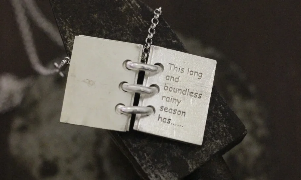 Close-up of Lazesoul Love Letter 925 sterling silver personalized book necklace, handmade with open notebook pendant engraved “This long and boundless rainy season has…,” on silver chain. Elegant custom jewelry gift.