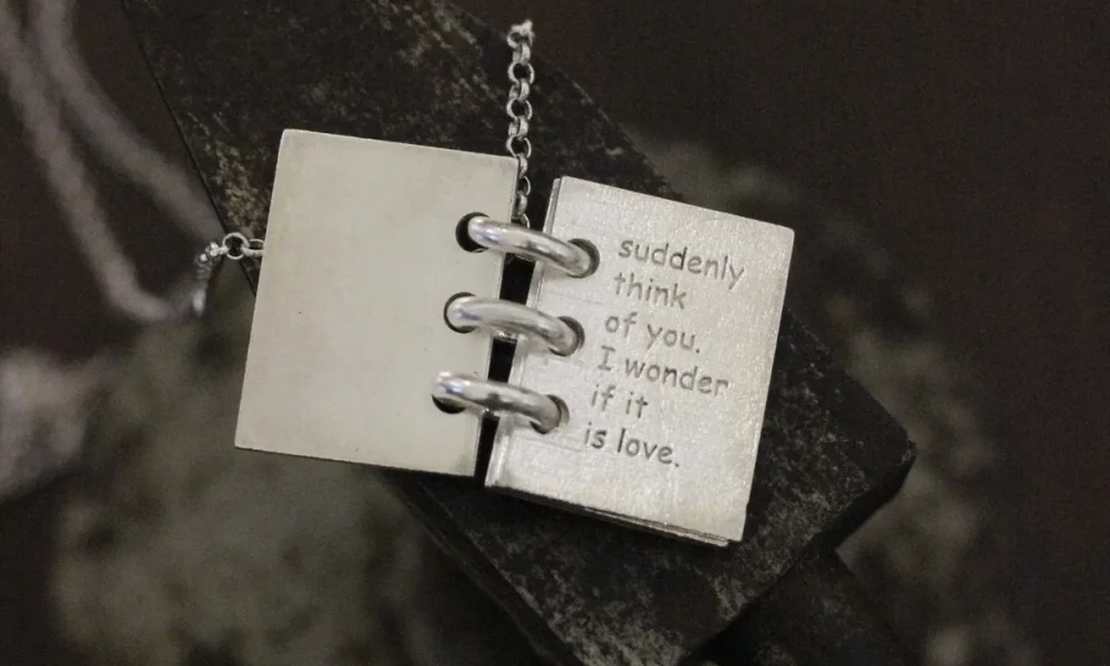 Close-up of Lazesoul Love Letter 925 sterling silver personalized book necklace, handmade with open notebook pendant engraved “suddenly think of you, I wonder if it is love,” on silver chain. Elegant custom jewelry gift.